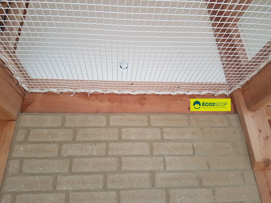 Brique de terre crue et filet de lecture sur vide sur séjour.